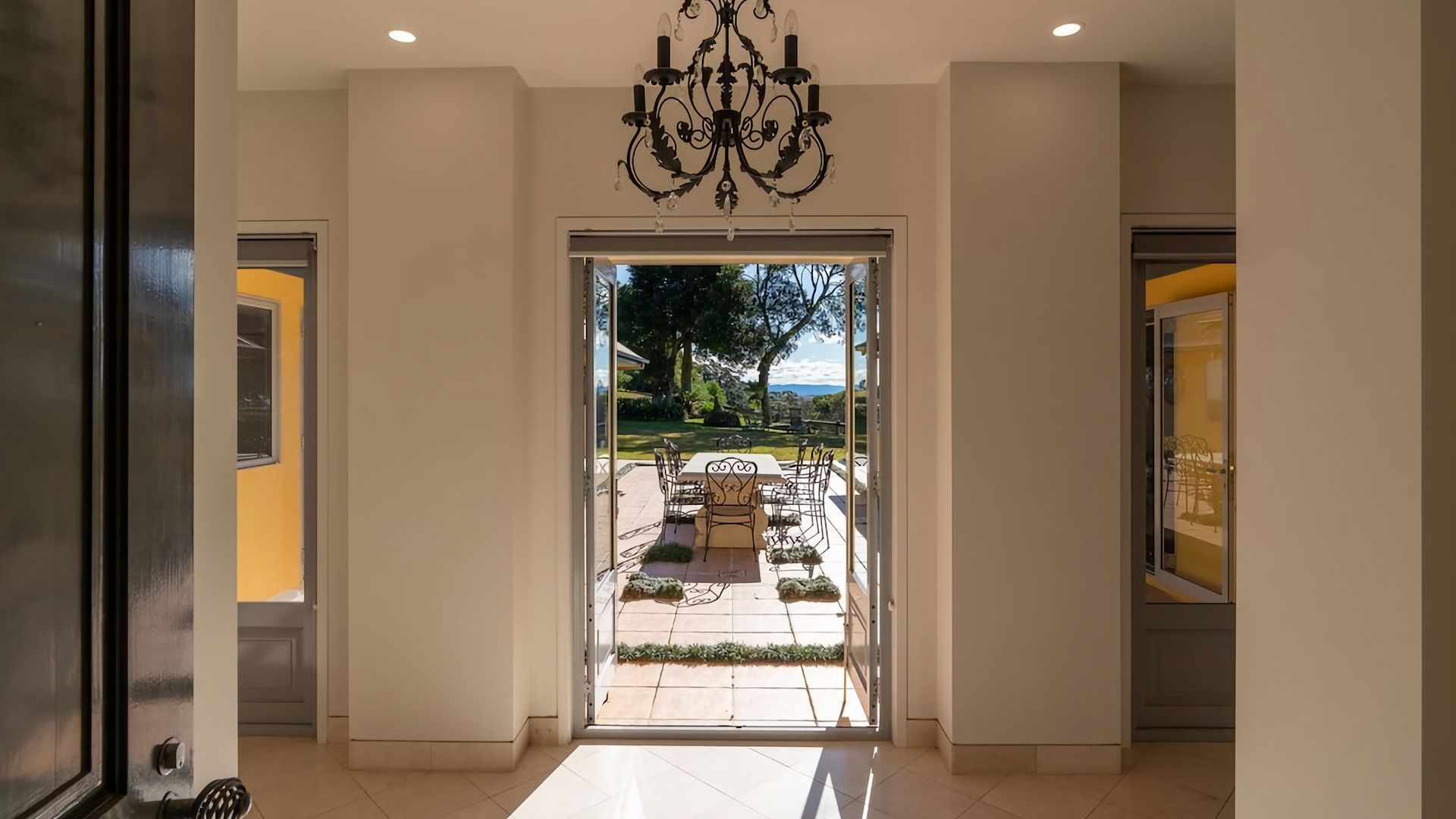 Entrada de hotel con un candelabro, un patio con mesa y sillas, y vistas al exterior.