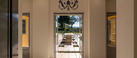 Ein Hotel Eingang mit einer Chandelüster, eine Terrasse mit Tisch und Stühlen sowie Blick ins Freie.