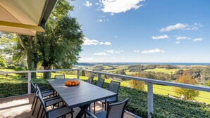An outdoor dining area with a table and chairs, overlooking a scenic landscape. - Flametrees ~ Enchanting holiday rental with absolutely stunning views of the coastline (Jamberoo)