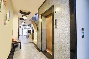 Un vestíbulo de hotel con pared de mármol, un ascensor, un banco y un candelabro.