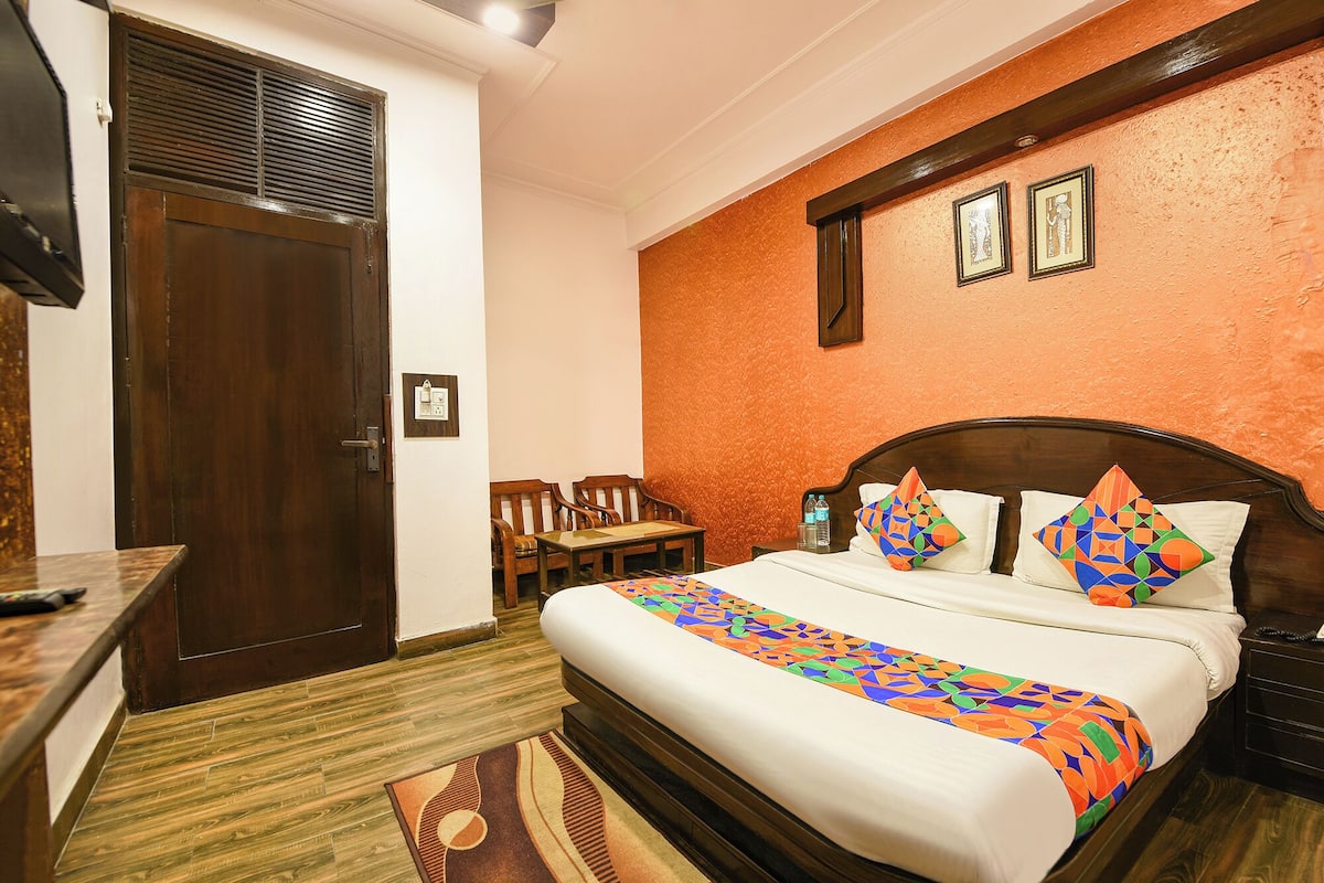 Een hotelkamer met een bed, een bureau, een stoel, een houten deur en een muur met twee ingelijste foto's.