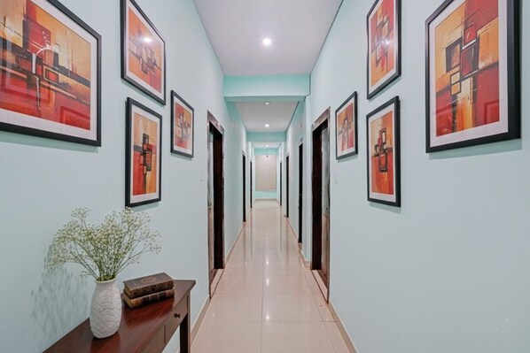 A hallway with framed artwork on the walls, a vase with flowers, and a wooden table. - Fabhotel Maa Tara (Danapur)