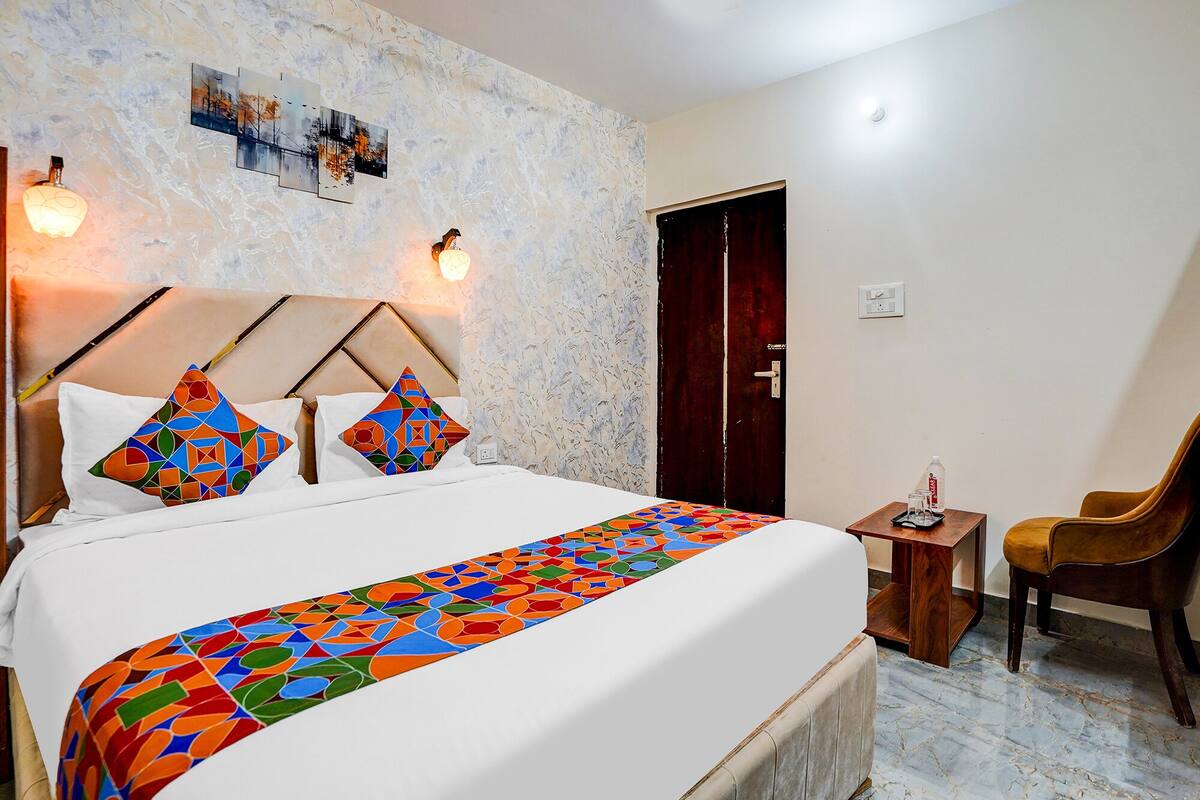 A hotel room with a bed, a wooden side table, a chair, and a door.