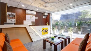 A hotel reception area with a marble counter, orange seating, and a view of the outdoor garden. - Fabhotel La Corporate Suite (Noida)