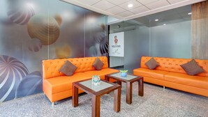 A reception area with two orange sofas, a glass wall, a welcome sign, and a decorative wall mural. - Fabhotel La Corporate Suite (Noida)