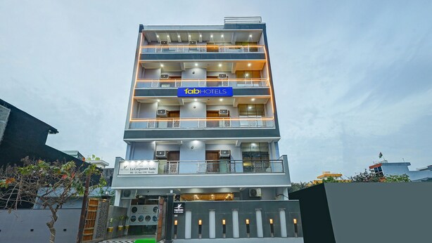 A multi-story hotel with balconies, a blue sign indicating it's a Tumb Hotels property, and a gated entrance with a green carpet. - Fabhotel La Corporate Suite (Noida)