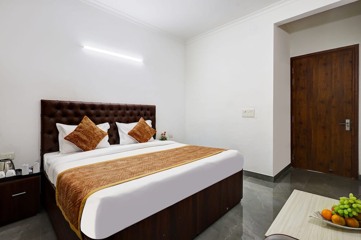 Habitación de hotel ordenada con una cama grande, un armario de madera, una mesita de noche y una cesta de frutas en el suelo.