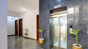 A hallway with a marble floor, two potted plants, a wooden door, and an elevator with a marble wall. - Fabhotel La Corporate Suite (Noida)