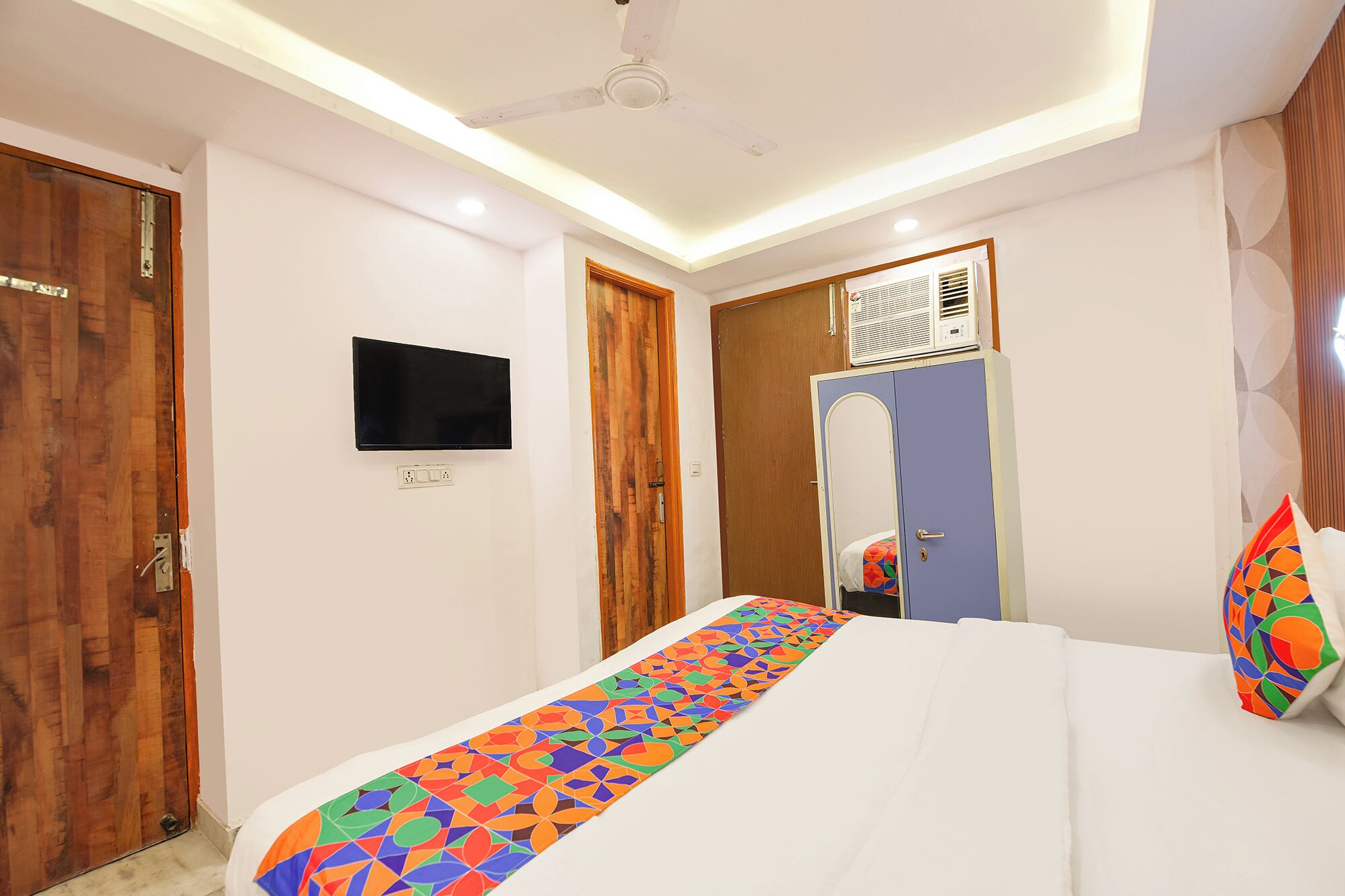 Habitación de hotel con cama, televisión montada en la pared, armario y ventilador de techo.
