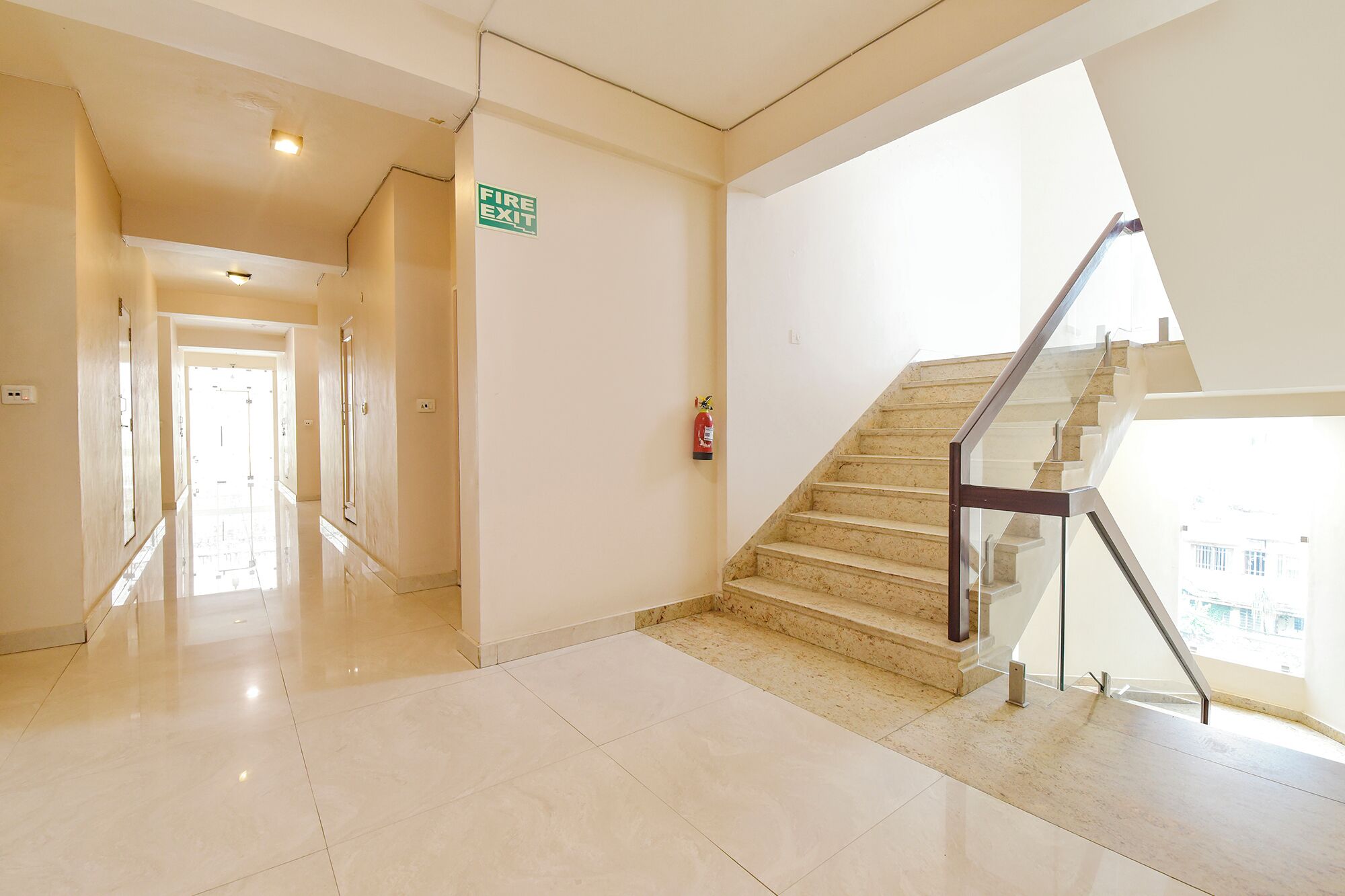 Un pasillo de hotel con un letrero de salida de incendios, un extintor y una escalera que conduce a un piso superior.