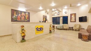 A hotel reception area with a marble floor, a reception desk, a seating area with chairs, a television mounted on the wall, and a clock. - Fabhotel Shikha (Jaipur)