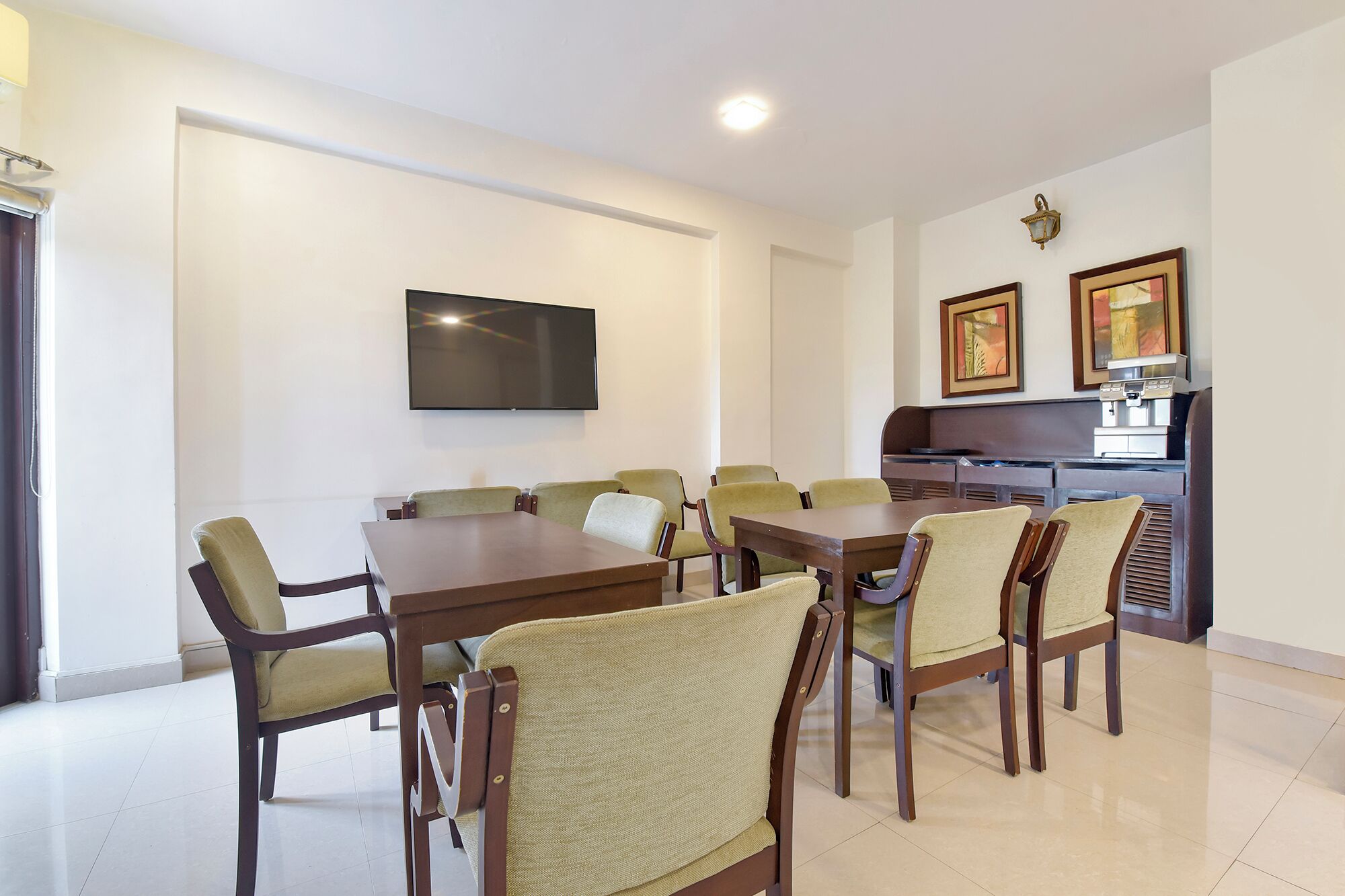 A dining area with a long table and chairs, a flat-screen TV mounted on the wall, and a coffee machine in the background.