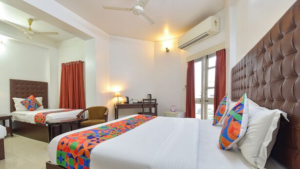 A hotel room with two beds, a desk, a chair, a lamp, and an air conditioning unit. - Fabhotel Shikha (Jaipur)