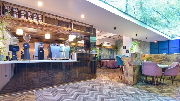 A modern restaurant with a herringbone floor pattern, wooden bar counter, and seating area with chairs and tables. - Fabhotel Shikha (Jaipur)