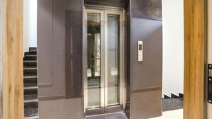 Ein Aufzug mit Glastür, Bedienfeld und einer Treppe zu einer anderen Etage.