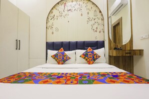 Cama com colcha estampada em padrão geométrico colorido e duas almofadas com desenhos semelhantes.
