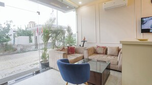 Ein modernes Wohnzimmer mit einem Glastisch, einem blauen Sessel und einem beigefarbenen Sofa mit gemusterten Kissen.