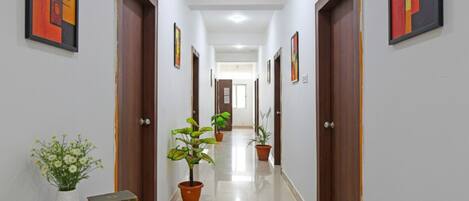 A hallway with wooden doors, potted plants, and framed artwork on the walls.