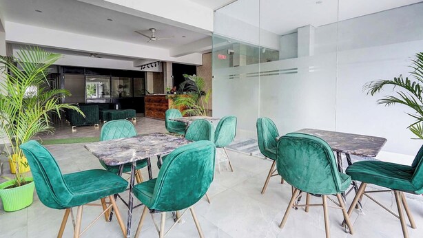 A modern indoor space with green upholstered chairs and marble tables, a reception area, and a glass partition. - Fabhotel The Glampoint (Noida)