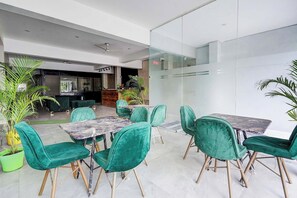 A modern indoor space with green upholstered chairs and marble tables, a reception area, and a glass partition. - Fabhotel The Glampoint (Noida)