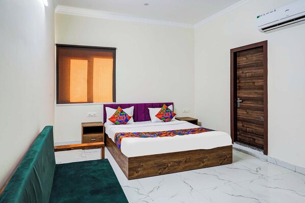 A bedroom with a bed, a nightstand, a dresser, a window, and an air conditioning unit.