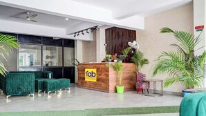 A hotel reception area with a wooden reception desk, green sofas, and potted plants. - Fabhotel The Glampoint (Noida)