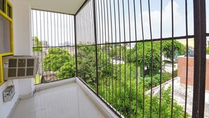 A balcony with metal railings, a white tiled floor, and an air conditioning unit. - Fabhotel The White Pepper (Faridabad)