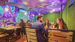 A restaurant with wooden tables and chairs, a green wall, and a ceiling with a colorful mural. - Fabhotel Western Inn (Chennai)