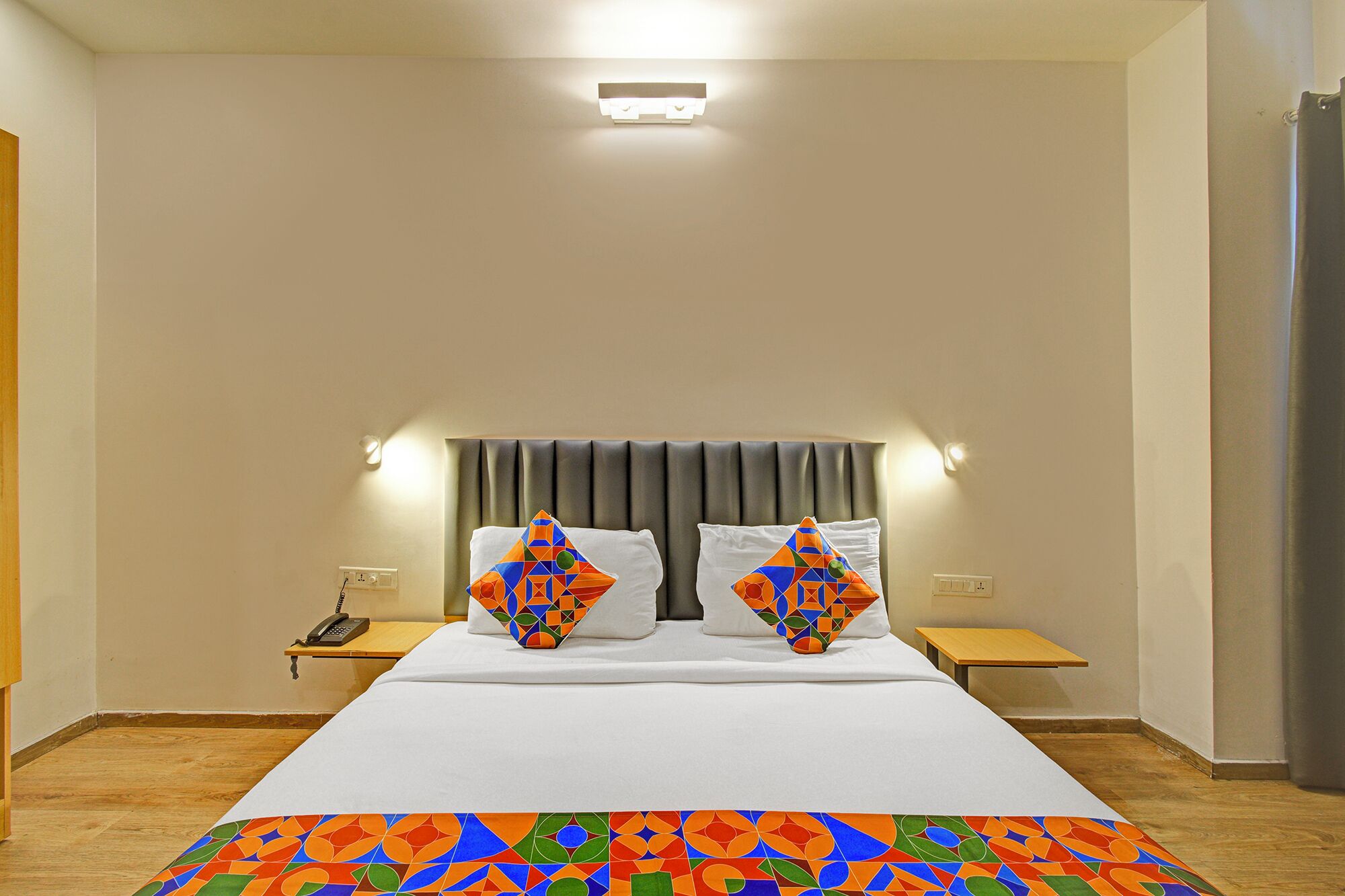 Una habitación de hotel con una cama, dos mesitas de noche, un teléfono y una cortina.