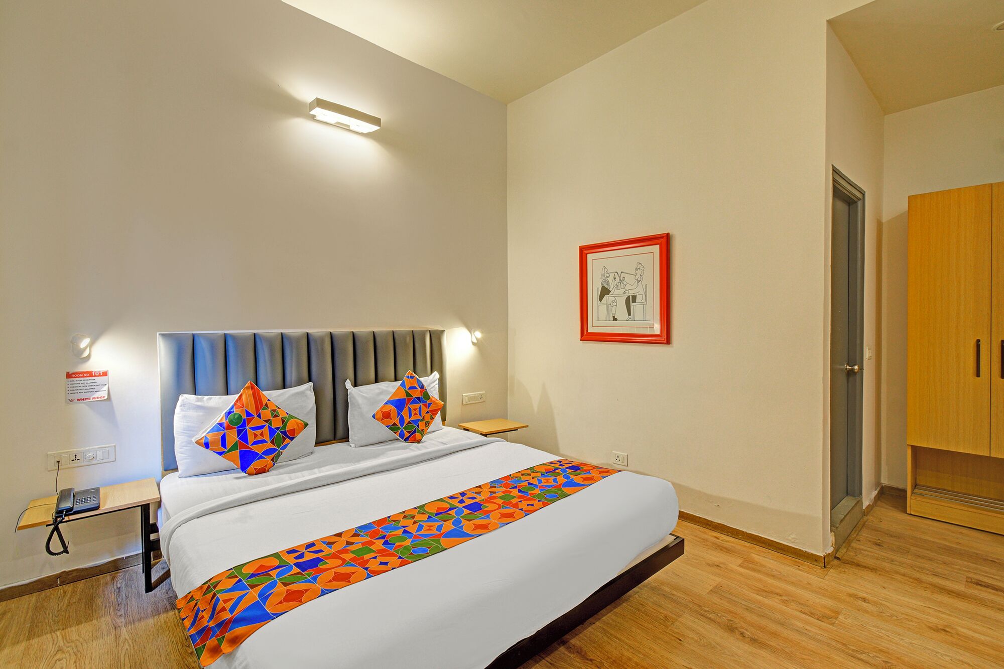 Ein Hotelzimmer mit Bett, Nachttisch und einem gerahmten Bild an der Wand.