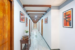 A hallway with wooden beams, framed artwork on the walls, and a marble floor. - Fabhotel Bridge (Ahmedabad)