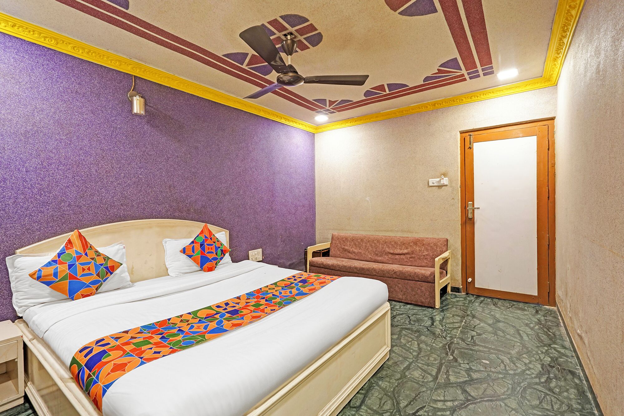 A hotel room with a bed, a chair, a ceiling fan, and a door.
