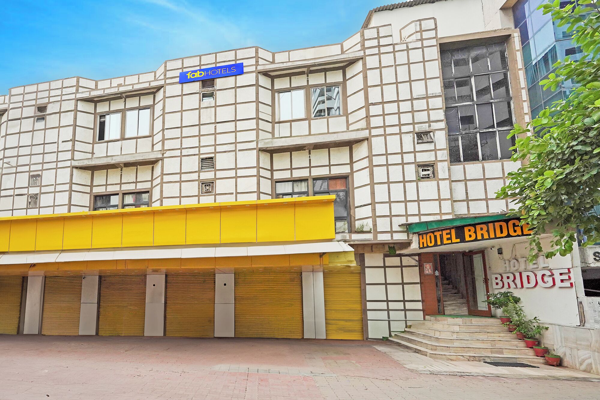 A building with a facade of square panels, a sign for 'fabHOTELS' at the top, a yellow awning, and a sign for 'HOTEL BRIDGE'.