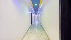 Un long couloir étroit, doté d’un sol carrelé et d’un plafond équipé de luminaires linéaires.