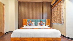 Une chambre d’hôtel avec un grand lit, une tête de lit en bois et un rideau à motifs.