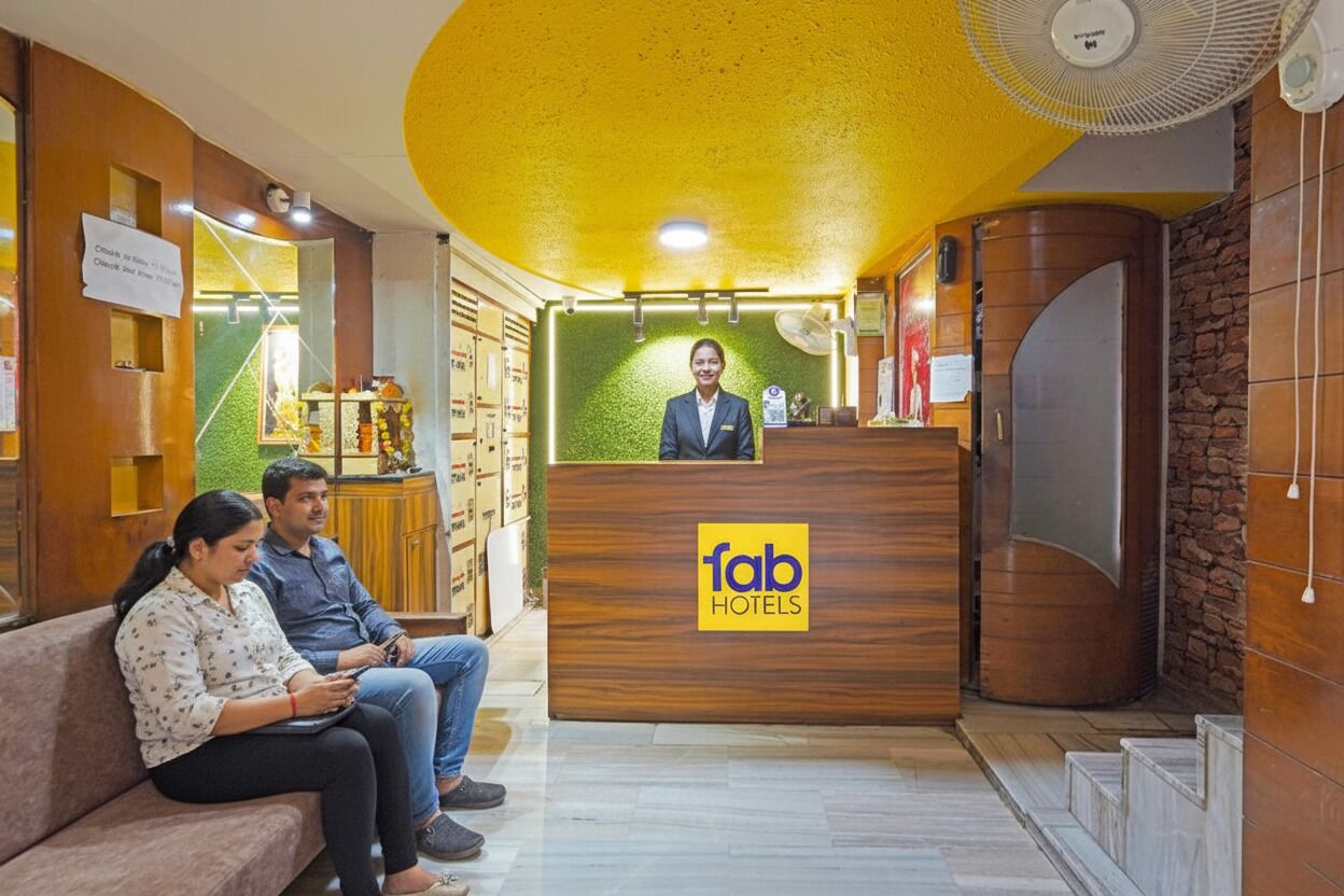 A hotel reception area with a wooden reception desk labeled "fab hotels," a waiting area with a sofa, and a fan on the ceiling.