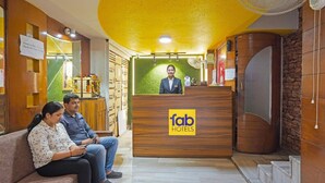 Un hall d’accueil d’hôtel avec un comptoir en bois portant l’inscription « fab hotels », un espace d’attente avec un canapé et un ventilateur au plafond.