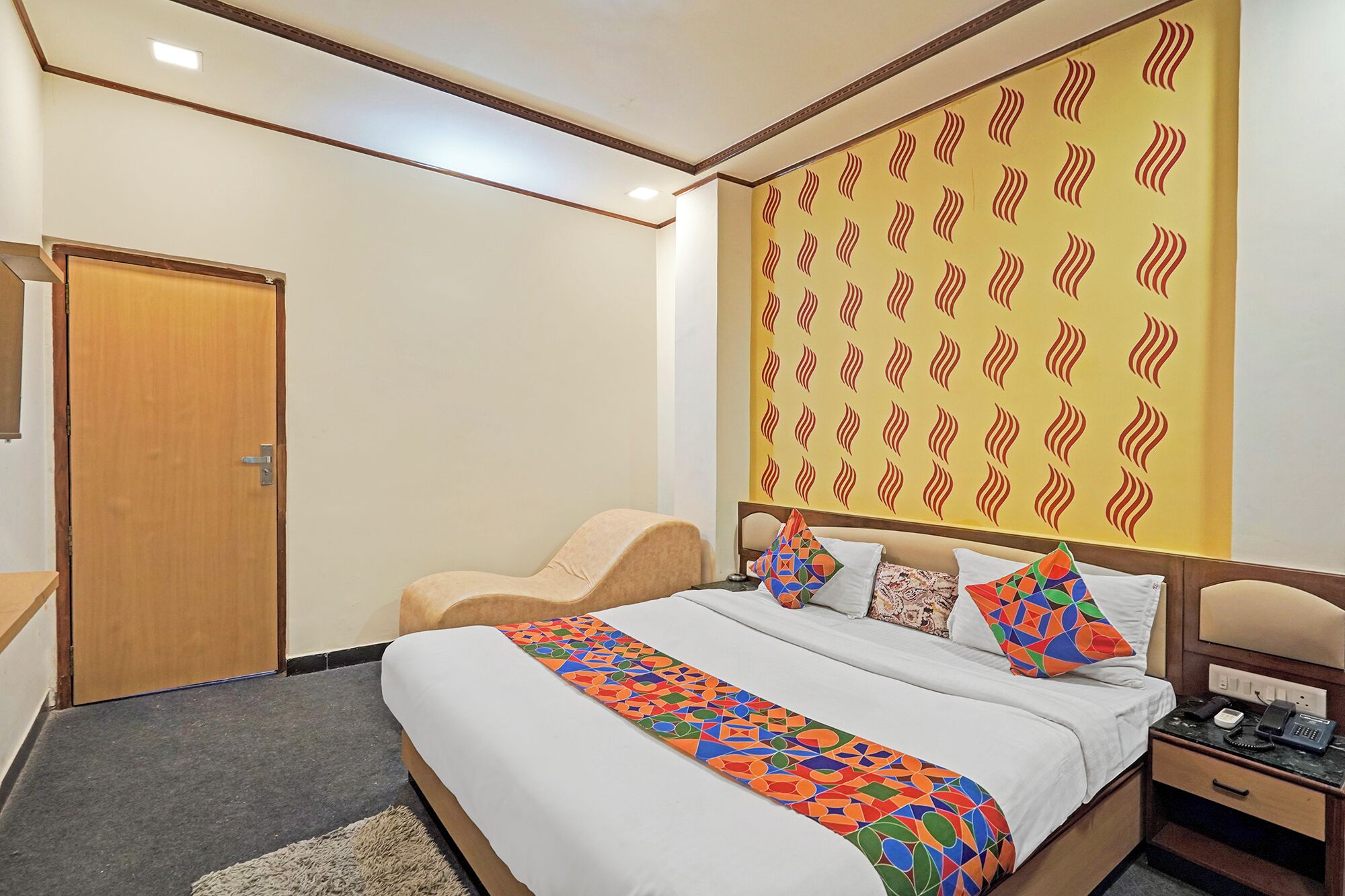 A hotel room with a bed, a desk, a chair, and a patterned wall.