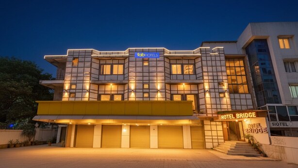 Un hôtel moderne, reconnaissable à son enseigne « Tab Hotels », à son entrée « Hotel Bridge » et à sa façade propre et bien éclairée.
