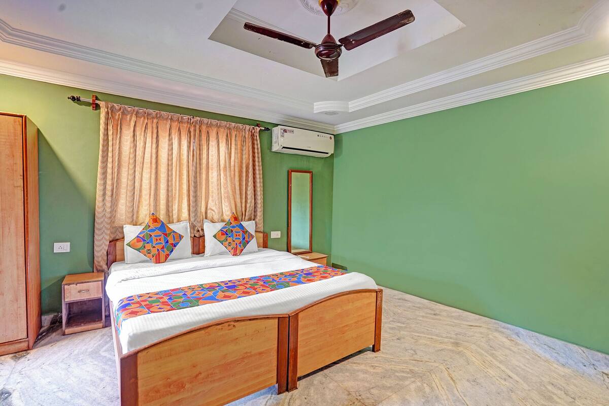 A bedroom with a bed, a ceiling fan, an air conditioning unit, a wardrobe, and a mirror.