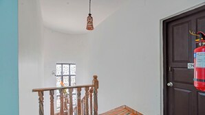 Μια σκάλα με ξύλινα στηρίγματα και ένα διακοσμητικό δάπεδο, που οδηγεί σε ένα δωμάτιο με μια σκούρα πόρτα και έναν πυροσβεστήρα τοποθετημένο πάνω της.