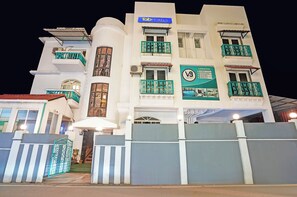 Un hôtel à plusieurs étages doté de balcons, une enseigne indiquant « fab hotels », et une autre enseigne « V9 Hotel » signalant la présence d’installations telles qu’une piscine et un restaurant.