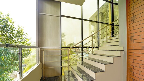 Un escalier moderne avec des rampes en verre et des marches en marbre, menant à un balcon d’où l’on peut admirer la verdure.