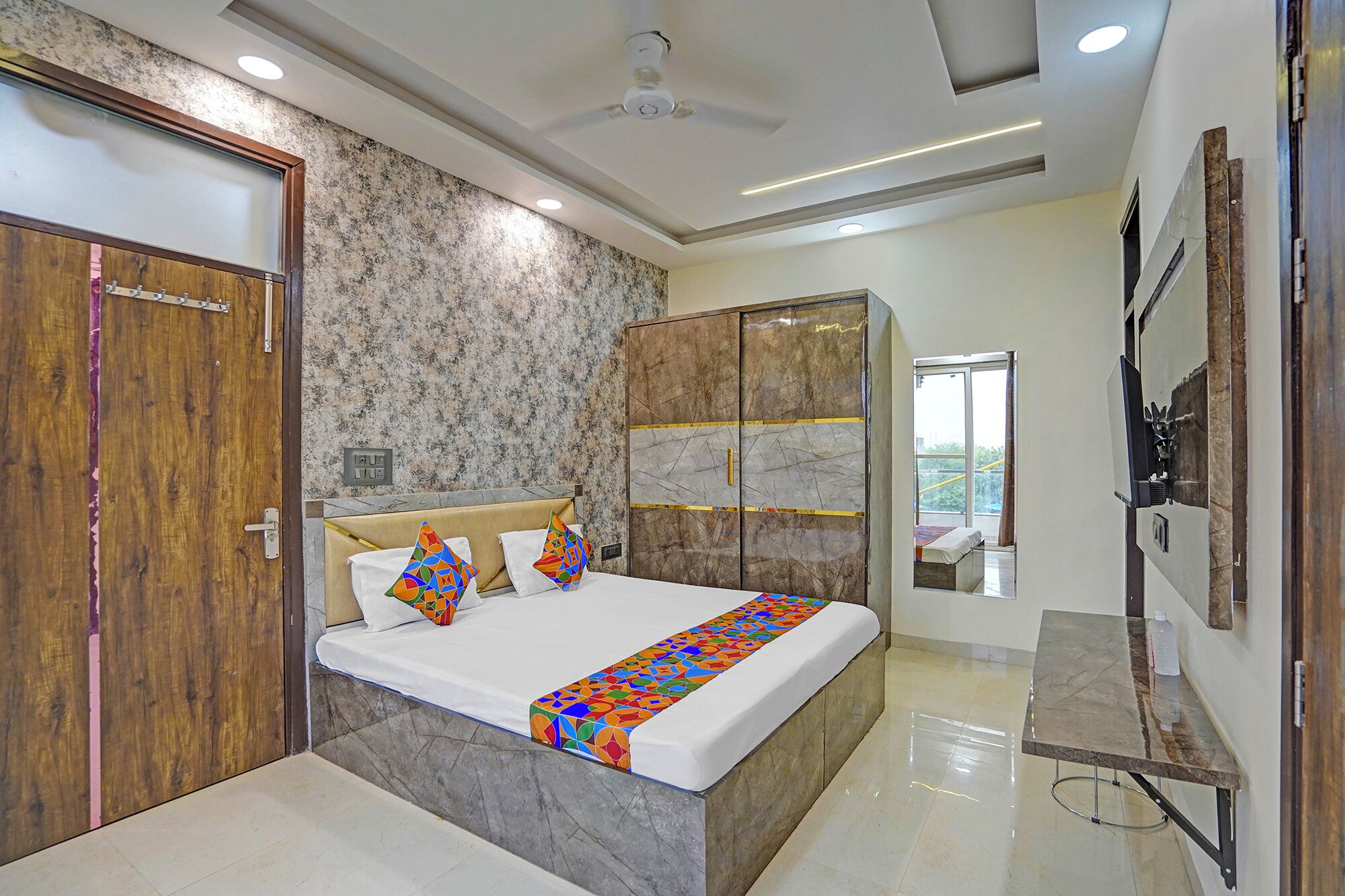 A modern bedroom with a bed, wooden wardrobe, and a TV mounted on the wall.