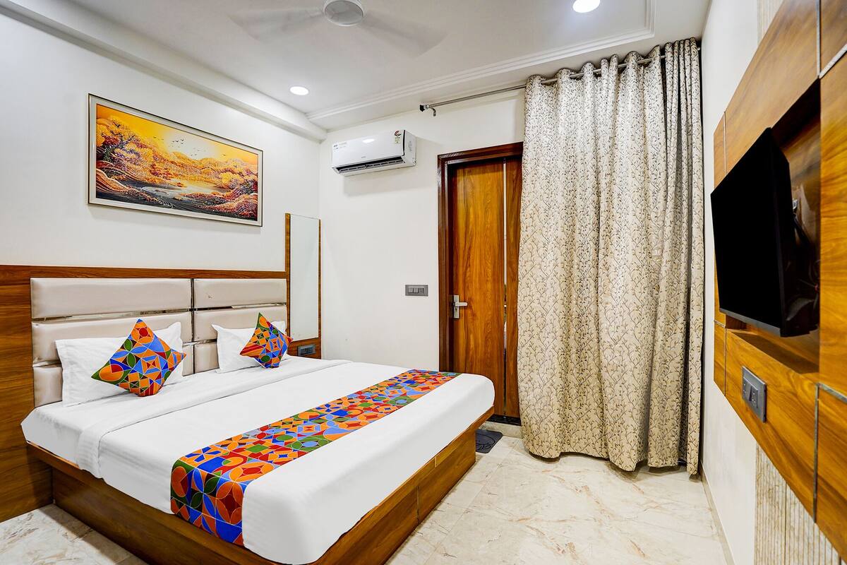 A hotel room with a bed, a TV, a painting on the wall, and a door.