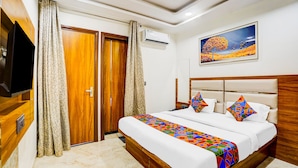 Una habitación de hotel con un armario de madera, un televisor, una cama con colcha de diseño geométrico y un cuadro de un árbol en la pared.