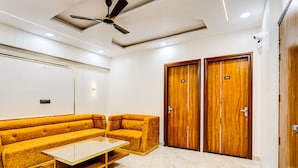 Una habitación de hotel moderna con sofá, una mesa de centro de vidrio, armarios de madera y un ventilador de techo.