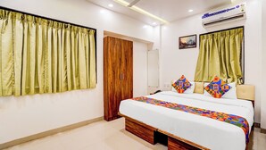 Quarto de hotel com cama, armário de madeira, ventoinha no teto e ar condicionado.