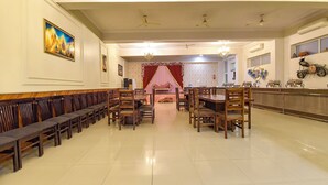 Un vaste hall doté de rangées de bancs et de tables en bois, d’un lustre, de ventilateurs de plafond et d’un rideau rouge en fond de scène.