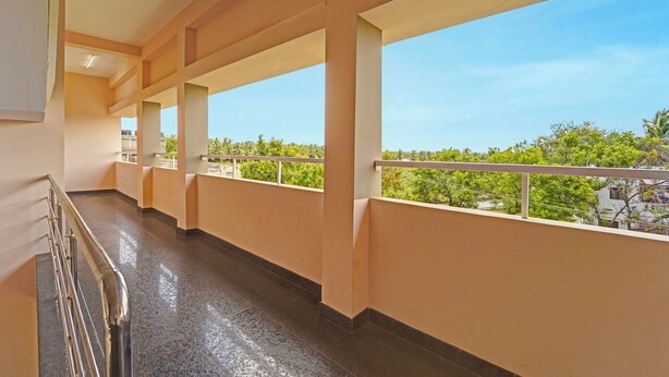 A corridor with large windows and a balcony, leading to a view of greenery and buildings. - Fabhotel Praneeth Residency (Sulur)